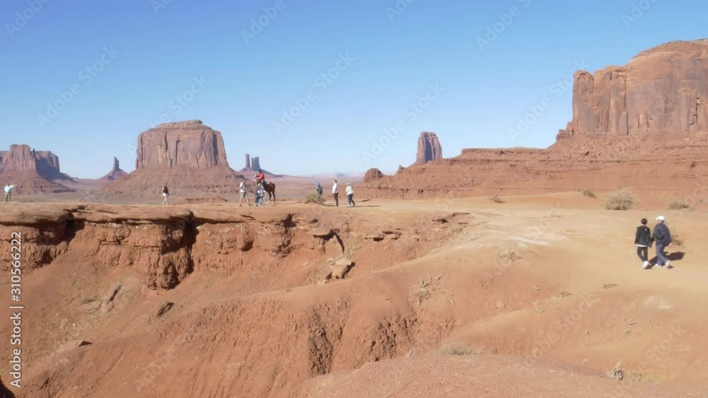 Monument Valley, Arizona, United States Of America - Tourist Guide Assisting A Man In Horse-Back Riding While Other Tourists Are Walking On A Sunny Day - Wide Shot Monument Valley, Arizona, United States Of America - Tourist Guide Assisting A Man In Horse-Back Riding While Other Tourists Are Walking On A Sunny Day - Wide Shot