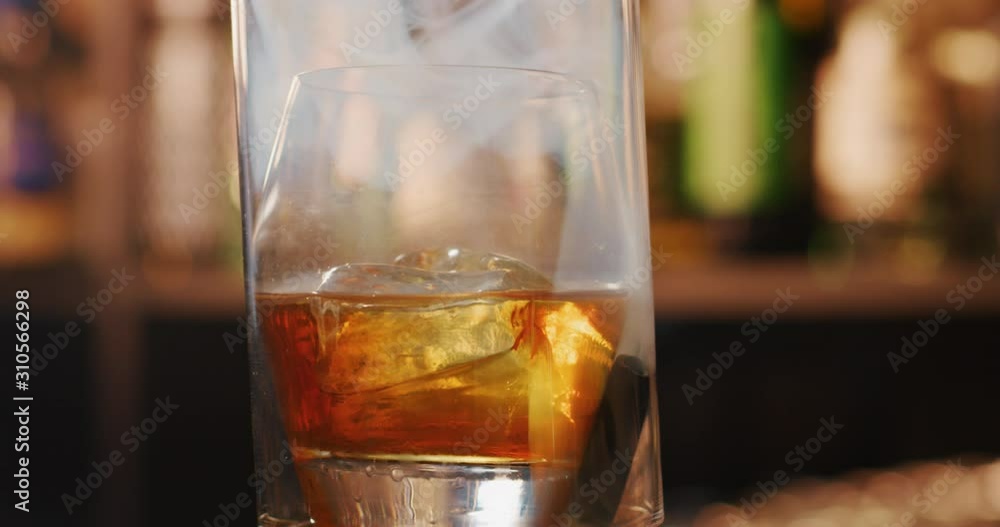Close up of a professional bartender is preparing an elite alcoholic cocktail with ice cubes and smoke to customers at the bar or disco club. Close up of a professional bartender is preparing an elite alcoholic cocktail with ice cubes and smoke to customers at the bar or disco club.
