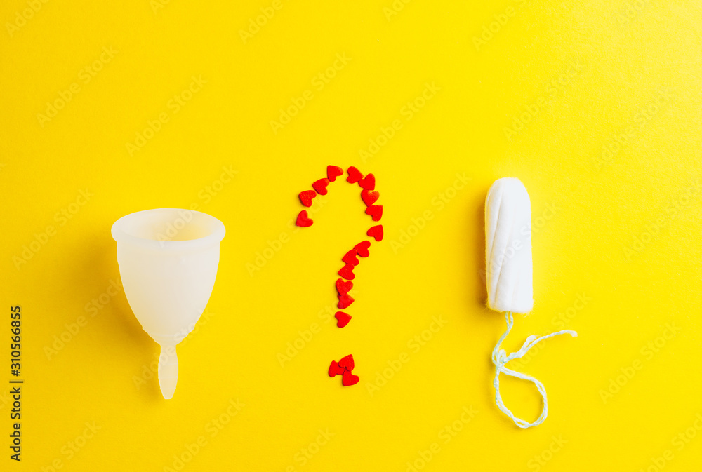 Fototapeta premium Menstrual cup, tampon and question from red hearts on yellow background. Alternative feminine hygiene product during the period. Women health concept. Flat lay. Copy space.