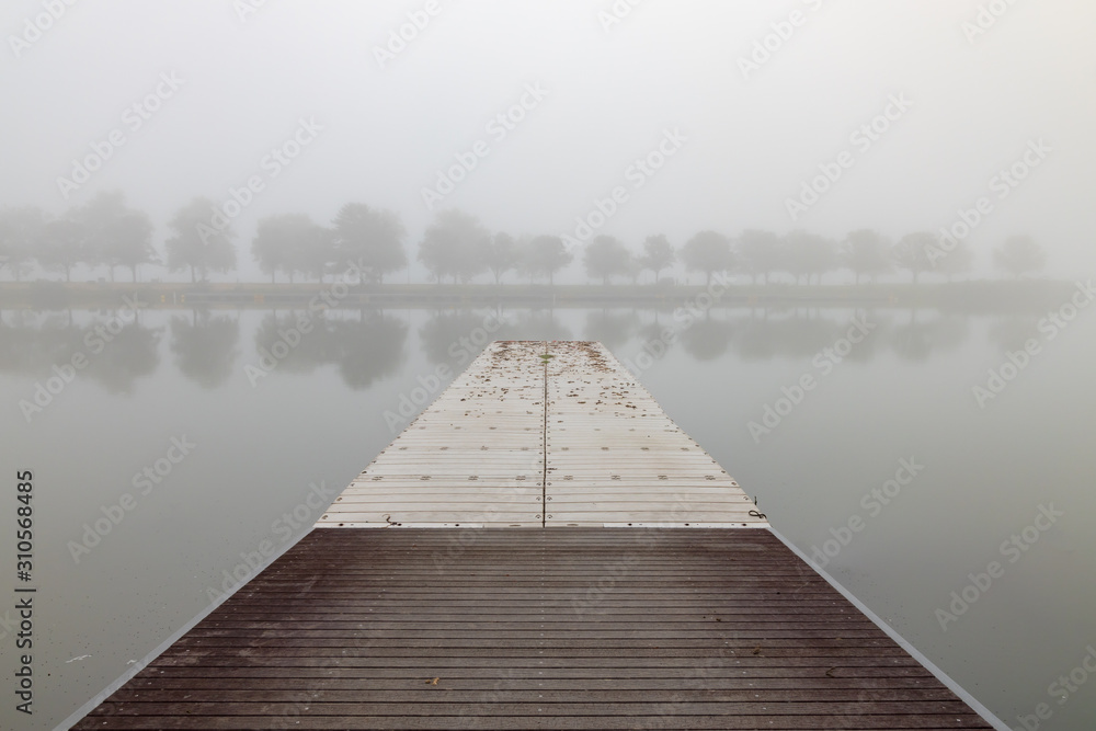 Fototapeta premium Floating fishing pier in the fog with treeline in background