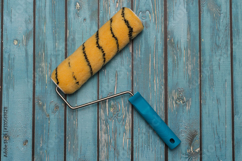 paint roller with a blue handle on a wooden blue background. Repair in the apartment.