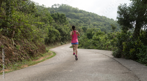 Sporty young woman in sportswear trail running on forest mountain path. Fitness girl jogging in Hong Kong