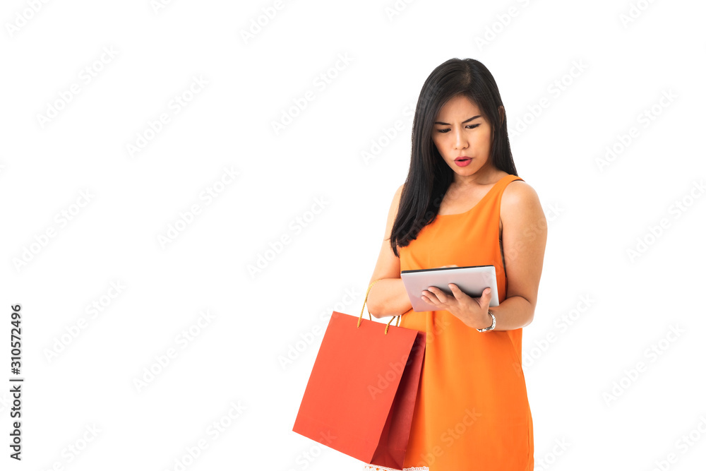 A beautiful Asian young woman wearing orange dress holding a tablet and a shopping bag looking frustrated or confuse in front of white isolated background. A beautiful Asian young woman wearing orange dress holding a tablet and a shopping bag looking frustrated or confuse in front of white isolated background.