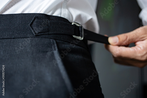 A man's hand is holding the edge of an elastic belt. Black trousers for men that can be stretched.