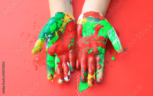Close-up baby hands with colorful fingers painted over red background.