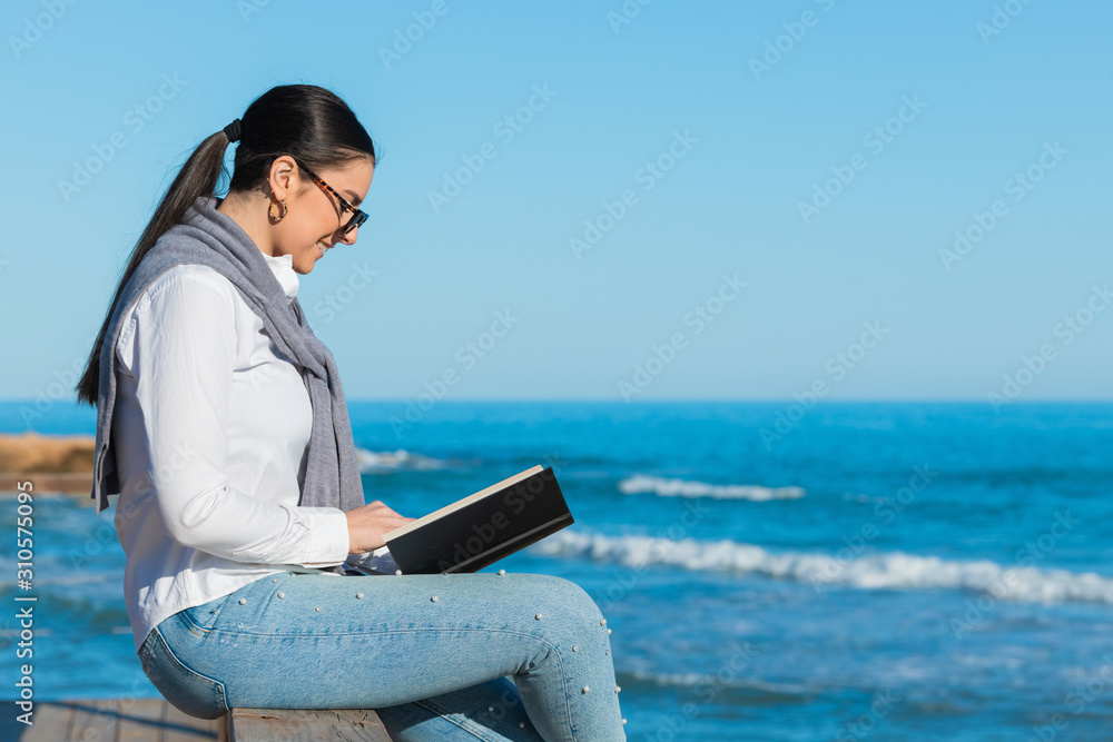 woman reads a book sitting on a wooden pathway railing