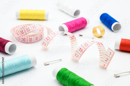 Sewing kit with measure tape, pins, colorful threads isolated on white background.