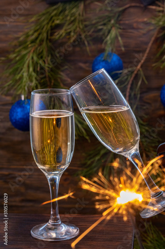 Glasses of champagne with bubbles on the background of Christmas decorations. Glasses touch during a festive toast and sparklers burn beautifully. Beautiful card.