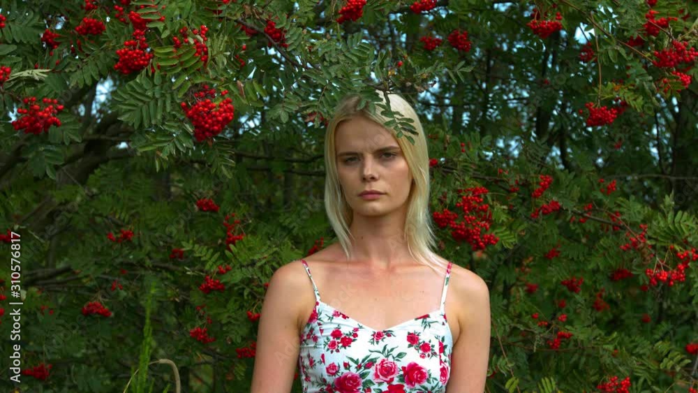 A woman standing underneath a tree with red berries, with a neutral expression A woman standing underneath a tree with red berries, with a neutral expression