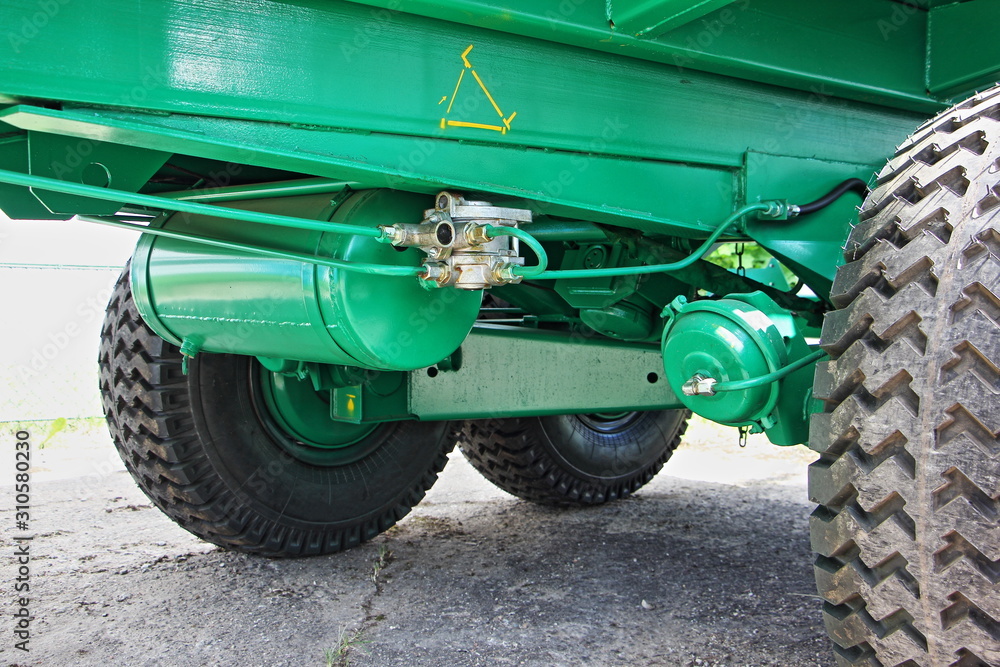 Pneumatic brakes on green tractor trailer frame close up, metal pipeline, distributor, air brake actuator mechanism and off road wheels Pneumatic brakes on green tractor trailer frame close up, metal pipeline, distributor, air brake actuator mechanism and off road wheels