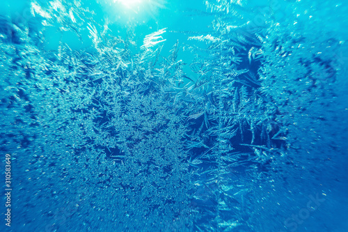 Ice freezes on glass in the cold winter season. Beautiful blue patterns left by frost on the window create the atmosphere of the New Year or Christmas holiday or other event.