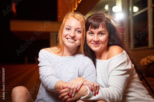 Two female friends on a city street at night. Girls and black background with light outdoors
