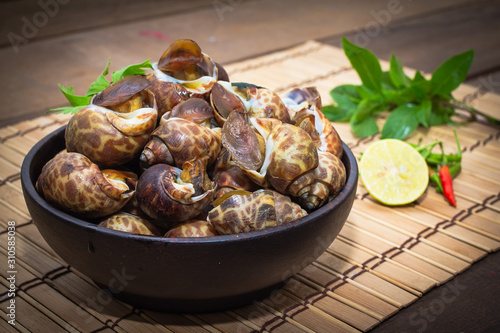 Boiled Babylonia areolata or shellfish on wooden bowl with lemon and chilli on table.Sea food photo