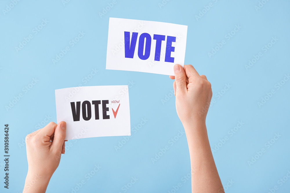 Hands holding papers with text VOTE on color background