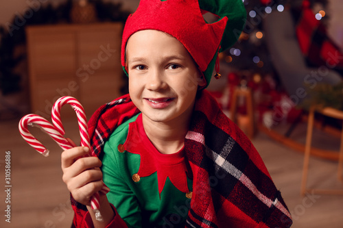 Little boy in costume of elf and with candy canes in room decorated for Christmas