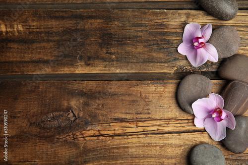 Stones with orchid flowers and space for text on wooden background, flat lay. Zen lifestyle