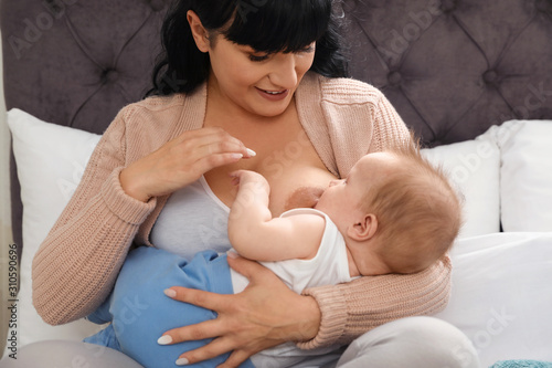 Woman breastfeeding her little baby on bed indoors photo