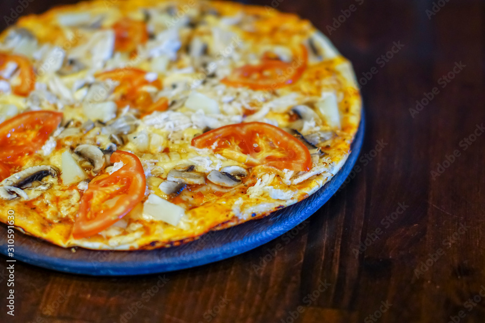 Delicious fresh pizza with meat, tomatoes and mushrooms served on a board on dark wooden table, close up Delicious fresh pizza with meat, tomatoes and mushrooms served on a board on dark wooden table, close up