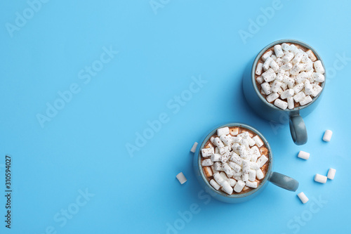 Delicious cocoa drink with marshmallows on light blue background, flat lay. Space for text