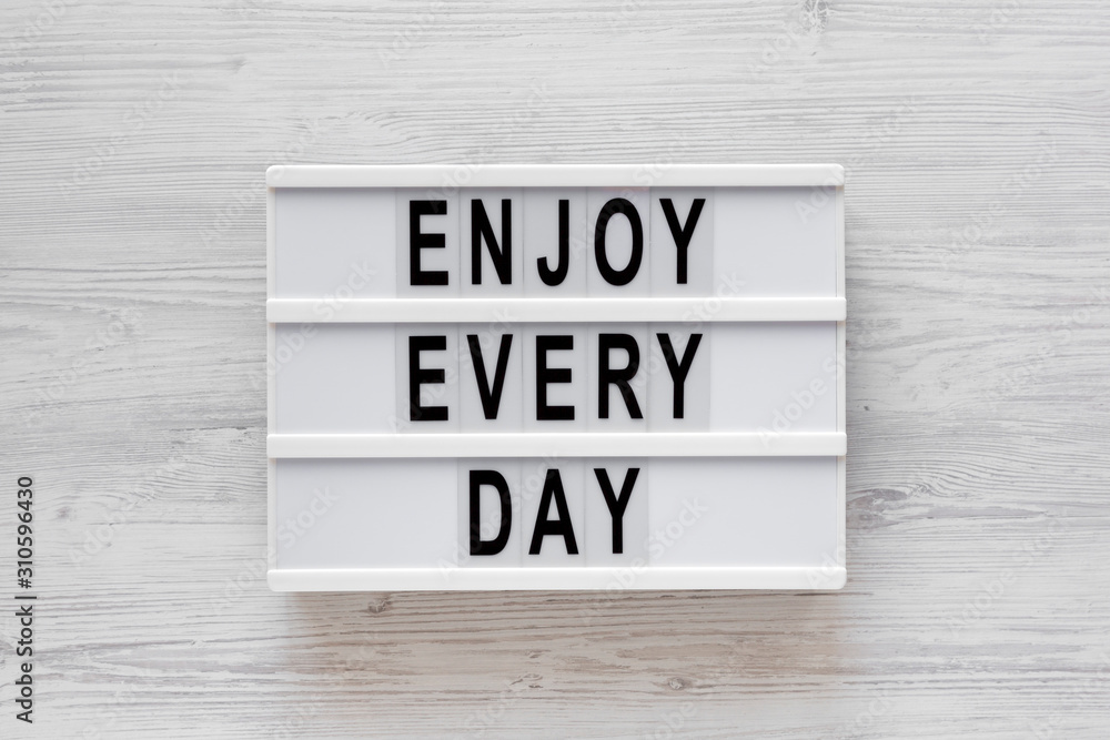 'Enjoy every day' words on a modern board on a white wooden background, top view. Overhead, from above, flat lay. Closeup. 'Enjoy every day' words on a modern board on a white wooden background, top view. Overhead, from above, flat lay. Closeup.