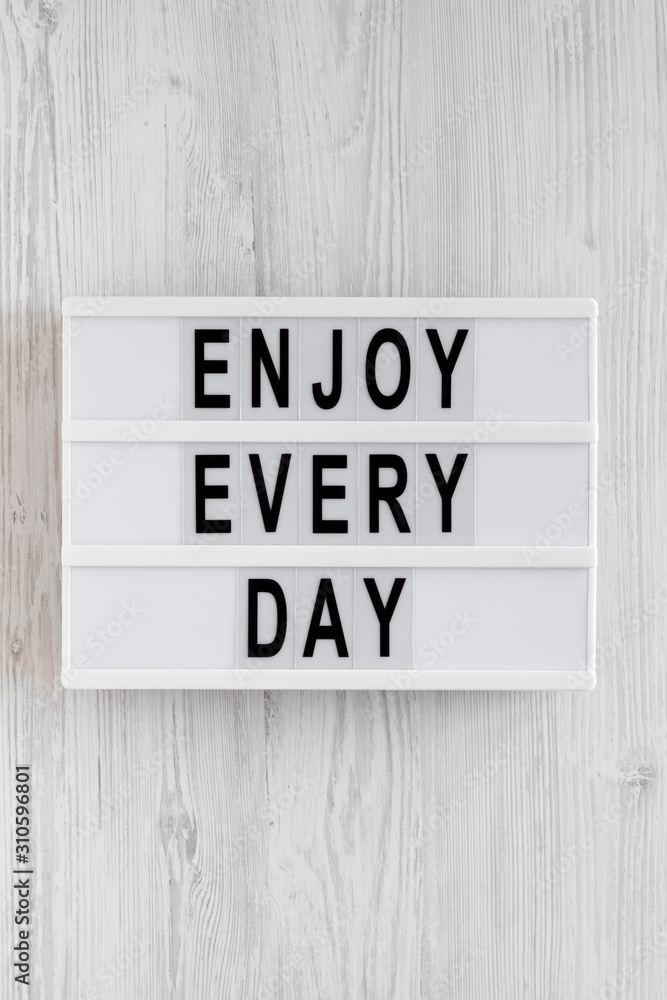 'Enjoy every day' words on a lightbox on a white wooden background, top view. Overhead, from above, flat lay. 'Enjoy every day' words on a lightbox on a white wooden background, top view. Overhead, from above, flat lay.
