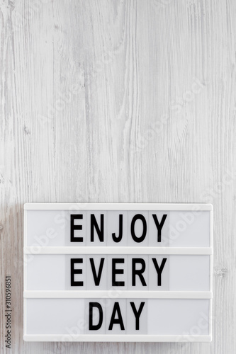 'Enjoy every day' words on a modern board on a white wooden surface, top view. Overhead, from above, flat lay. Copy space.