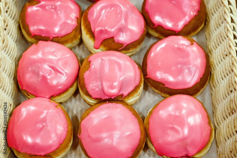 Fresh baked berliner, krapfen with pink glaze. Glazed donuts in basket in bakery, delicious pastries in showcase. Pastry shop with buns. Sweet dessert Fresh baked berliner, krapfen with pink glaze. Glazed donuts in basket in bakery, delicious pastries in showcase. Pastry shop with buns. Sweet dessert