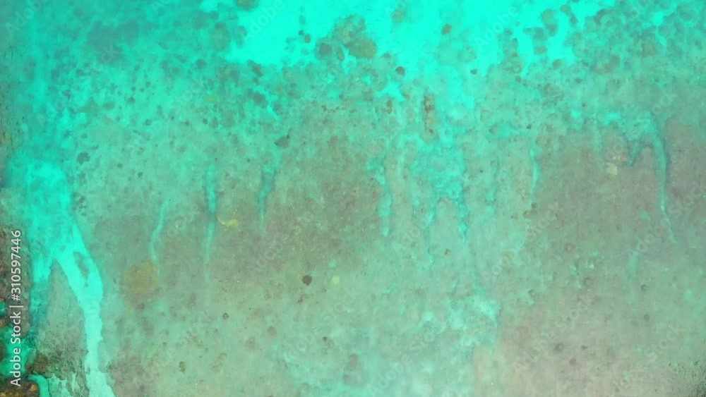 Drone hover above blue lagoon surface showing bottom relief through clear water Drone hover above blue lagoon surface showing bottom relief through clear water
