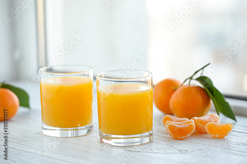 Glasses of fresh tangerine juice and fruits on white wooden table
