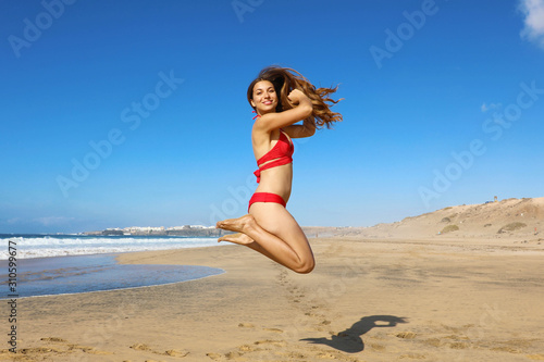 Carefree healthy bikini woman jumping on the beach. Happy smiling girl doing a jump of freedom and happiness in a free body on holidays. Weight loss success healthy lifestyle concept.