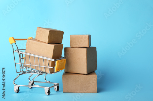 Shopping cart and boxes on light blue background, space for text. Logistics and wholesale concept