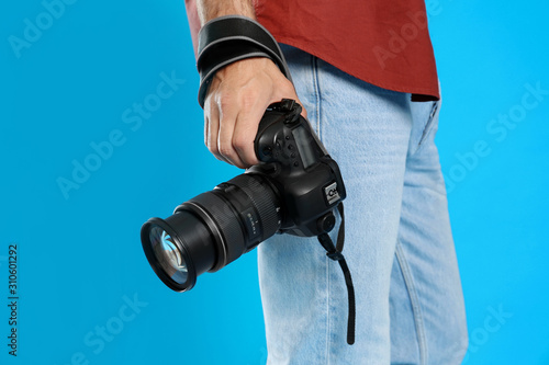 Professional photographer with modern camera on light blue background in studio, closeup