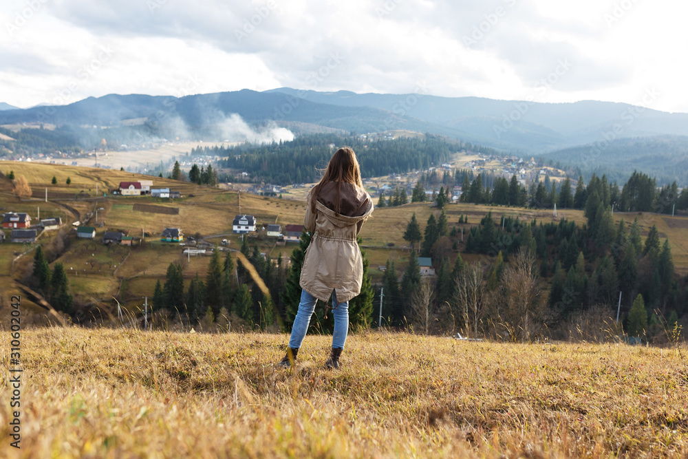 The young woman in the cozy sweater is enjoying the landscape from the foggy mountain