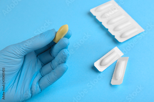 Woman holding suppository on light blue background, closeup. Hemorrhoid treatment