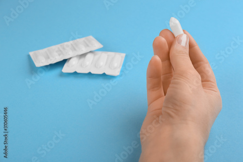 Woman holding suppository on light blue background, closeup. Hemorrhoid treatment photo