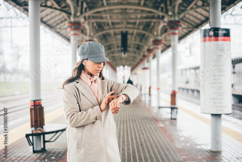 Woman standing on a train platform and looking at her watch. Girl is wating a train in a trian station at Europe. photo