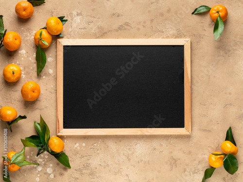 Wooden frame with empty black space (field) to write text, menu, time table or any words. Tangerines (oranges) with green leaves. Brown beige background. Design frame or template.