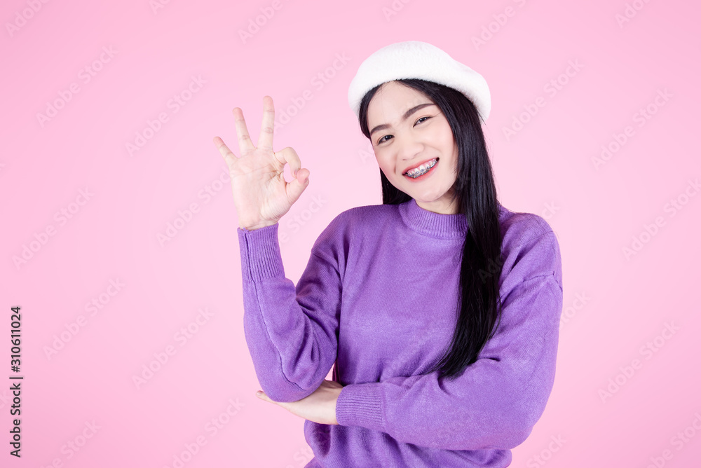 Happy Asian woman wearing purple sweater with OKAY sign language on pink background.
