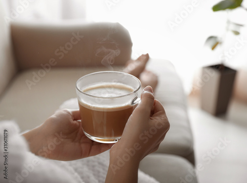 Fototapet Woman with cup of hot drink on sofa at home in morning, closeup