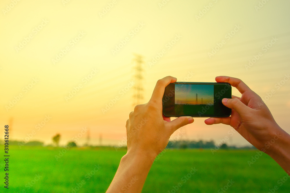 Hand holding smartphone take photo with beautiful view high voltage post with rice field on Sunlight