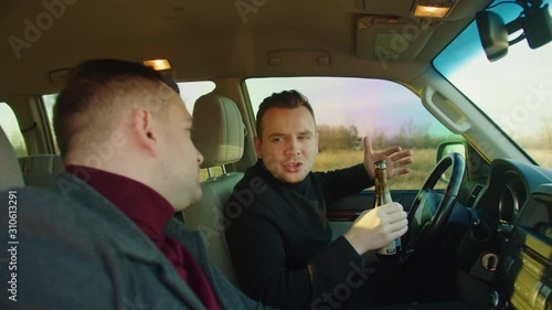 Scene in car .Two men are sitting in the car with bottles of beer, talking and laughing before the trip. Alcohol cancept and idea . the camera is on the side and behind the secondary glass photo