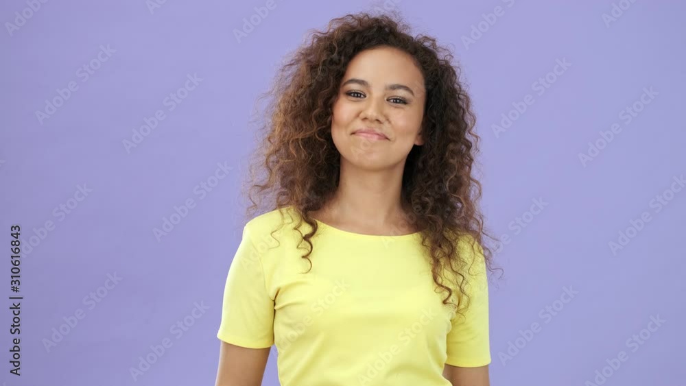 Positive african young woman in yellow t-shirt pointing and shaking her head approvingly while looking at the camera over purple background isolated Positive african young woman in yellow t-shirt pointing and shaking her head approvingly while looking at the camera over purple background isolated