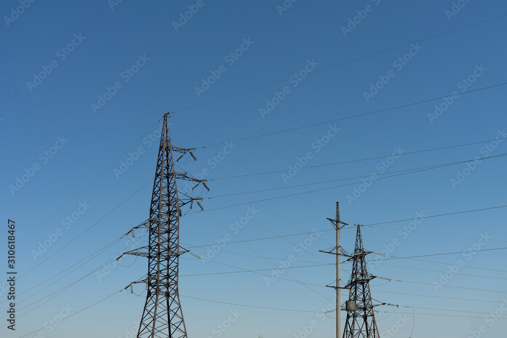 Fototapeta premium High voltage lines and power pylons in the industrial area on a Sunny day with a clear blue sky.