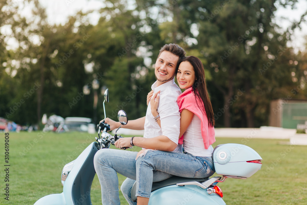 Good-looking girl with long hairstyle posing with shy smile on scooter. Glad young man in casual clothes sitting on bike with attractive lady on trees background. Stock Photo | Adobe Stock Good-looking girl with long hairstyle posing with shy smile on scooter. Glad young man in casual clothes sitting on bike with attractive lady on trees background. Stock Photo | Adobe Stock