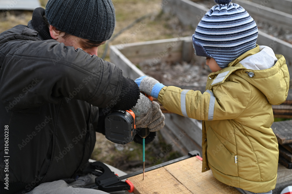 a father and a young son together make a construction, bed for plants, of wooden boards with a screwdriver. family hobby a father and a young son together make a construction, bed for plants, of wooden boards with a screwdriver. family hobby