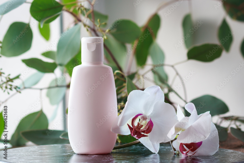 Cosmetic bottle with green leaves of eucalyptus and orchids. Blank label mock-up. Cosmetic bottle with green leaves of eucalyptus and orchids. Blank label mock-up.