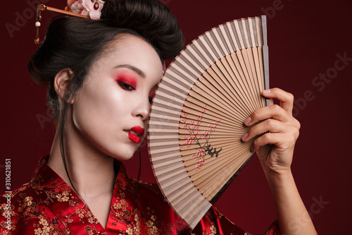 Image of young geisha woman in japanese kimono holding wooden hand fan