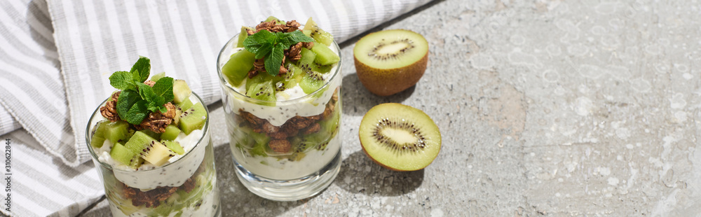 fresh granola with kiwi and yogurt on grey concrete surface with striped napkin, panoramic shot fresh granola with kiwi and yogurt on grey concrete surface with striped napkin, panoramic shot