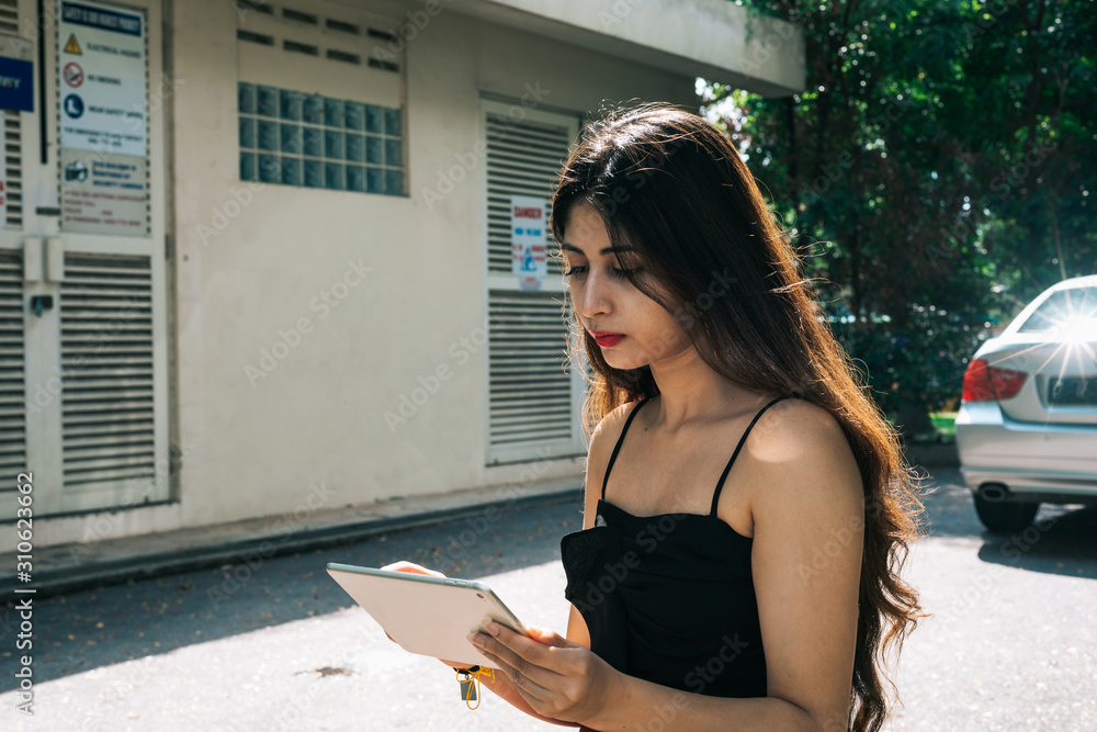 Obraz premium One long hair Indian girl holding and using mobile touch screen device tablet at outdoor park