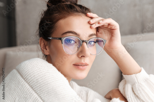 Image of lovely young woman in eyeglasses resting on sofa at home